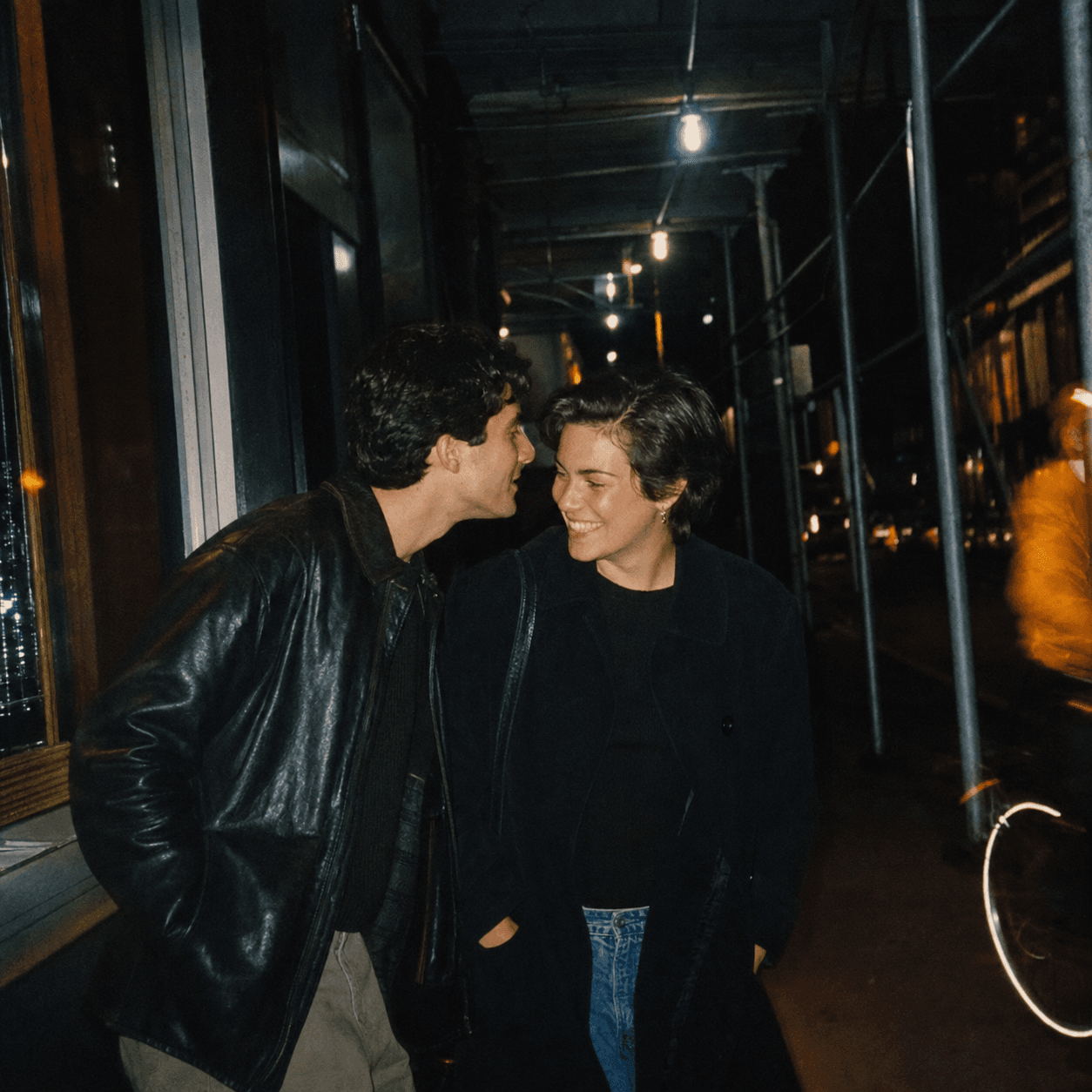Two people sharing a close moment under sidewalk scaffolding